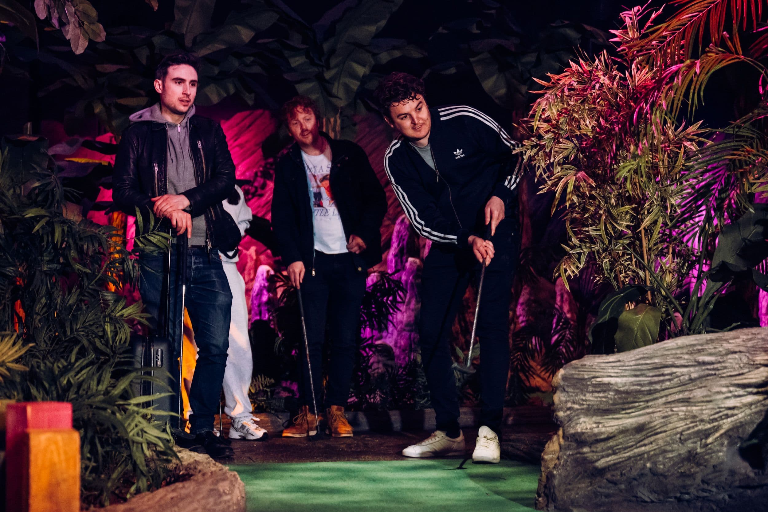 Three young male adults playing golf.