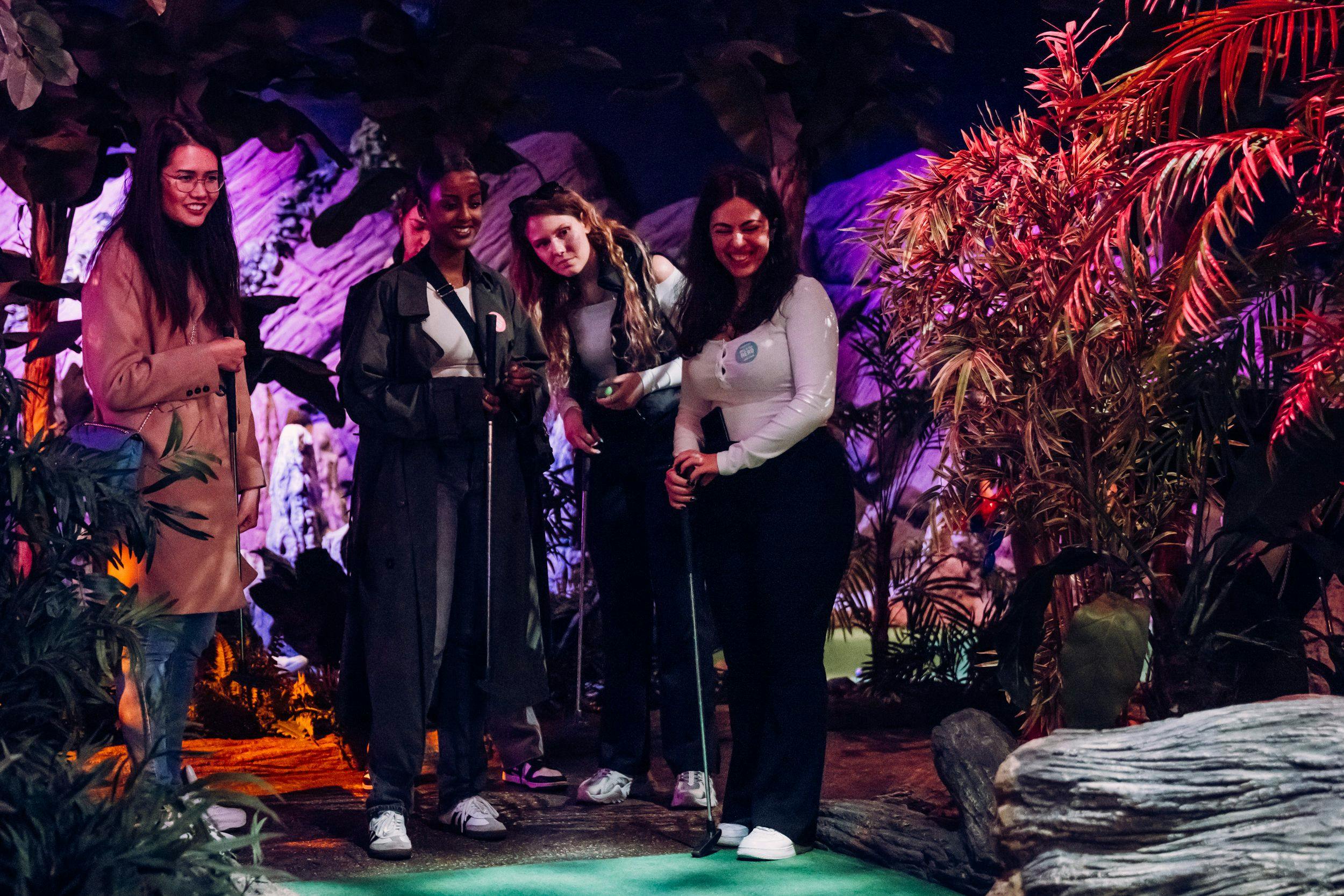 Five women laughing and playing mini golf
