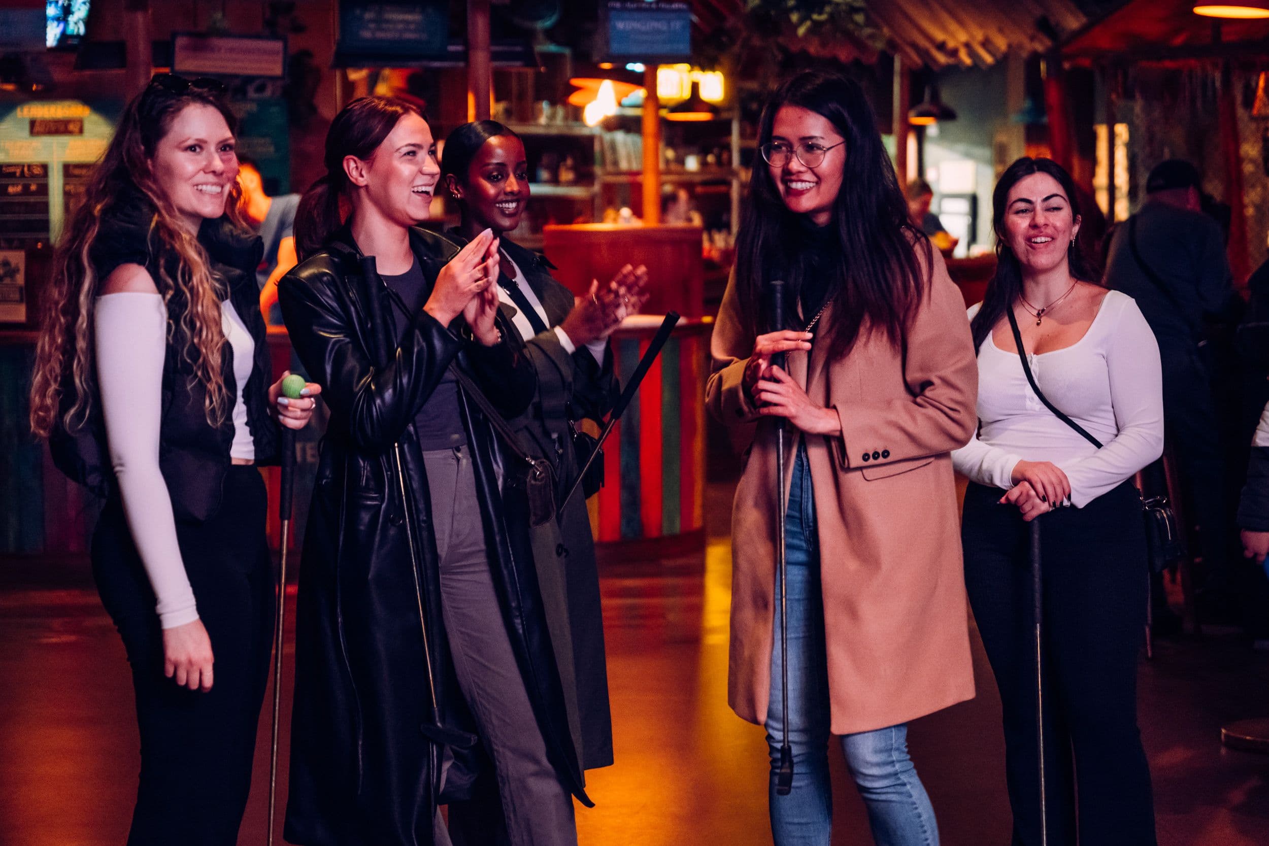 A group of 5 women laughing while playing mini golf.