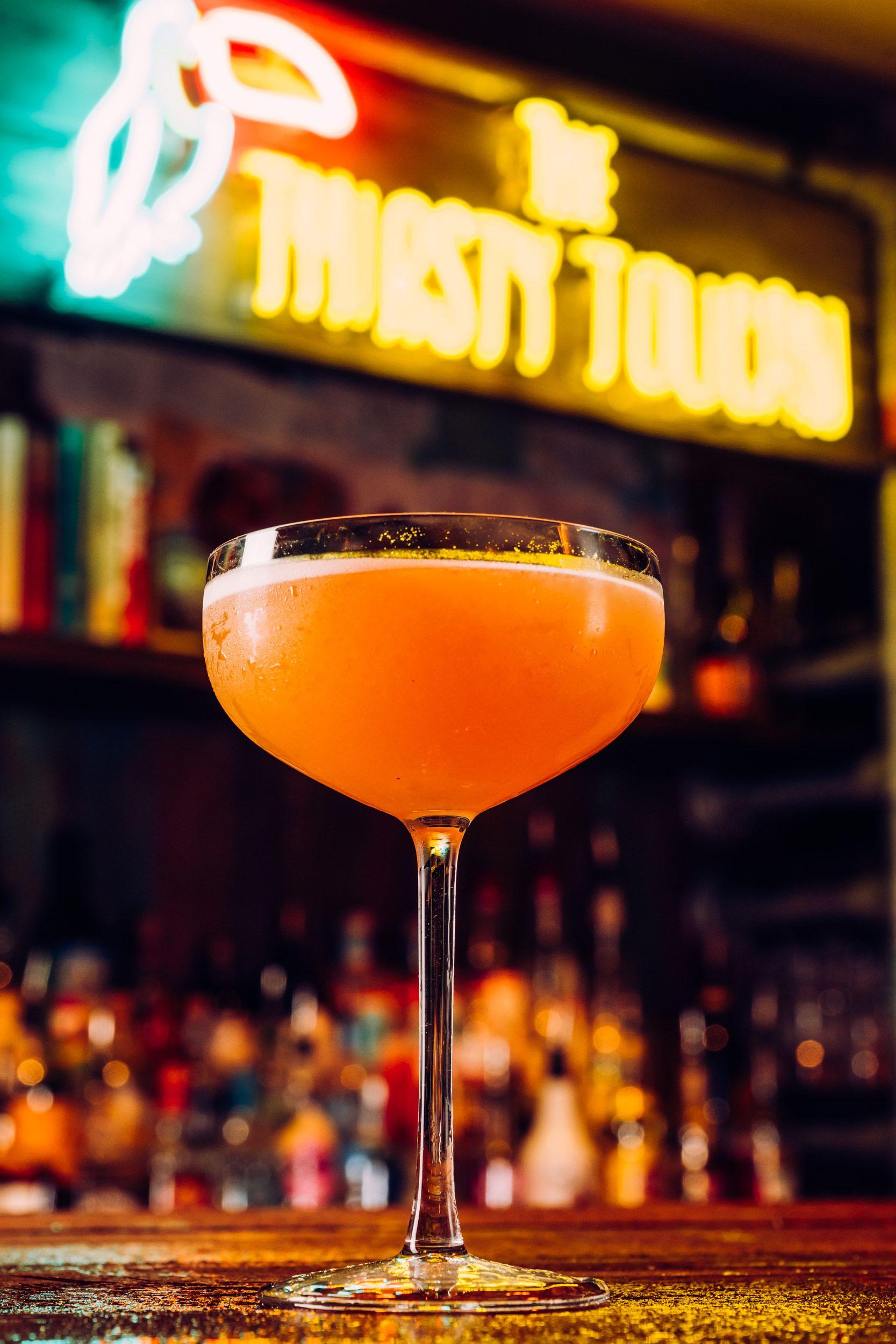 A martini cocktail positioned in front of the Thirsty Toucan logo.