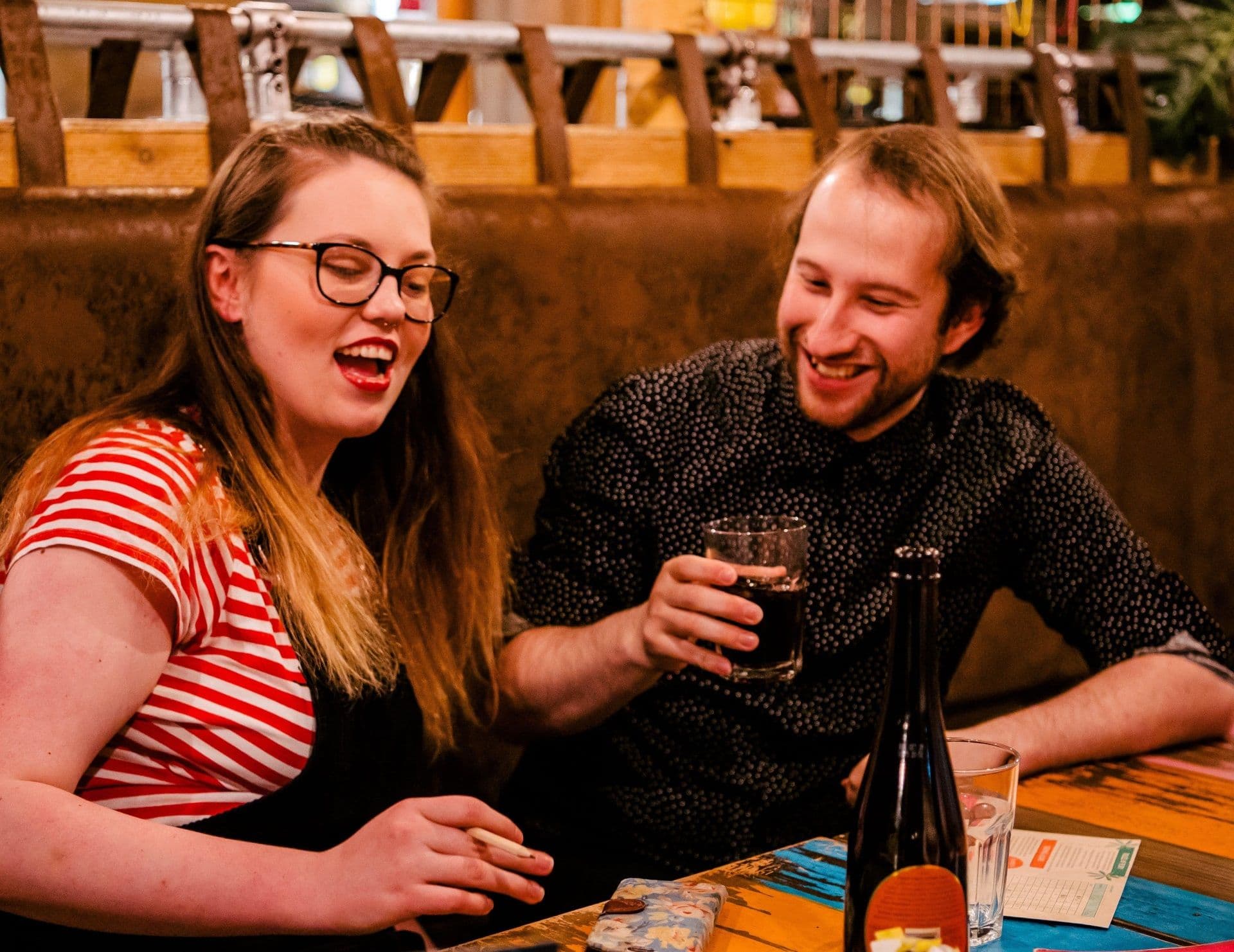 A young couple laughing and sharing drinks.