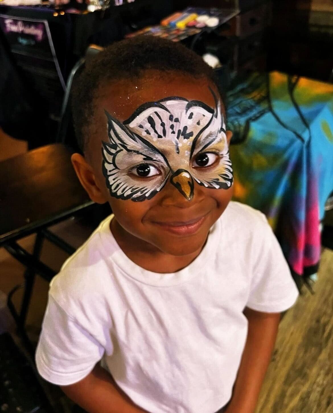 A child smiling with her face painted like an owl.