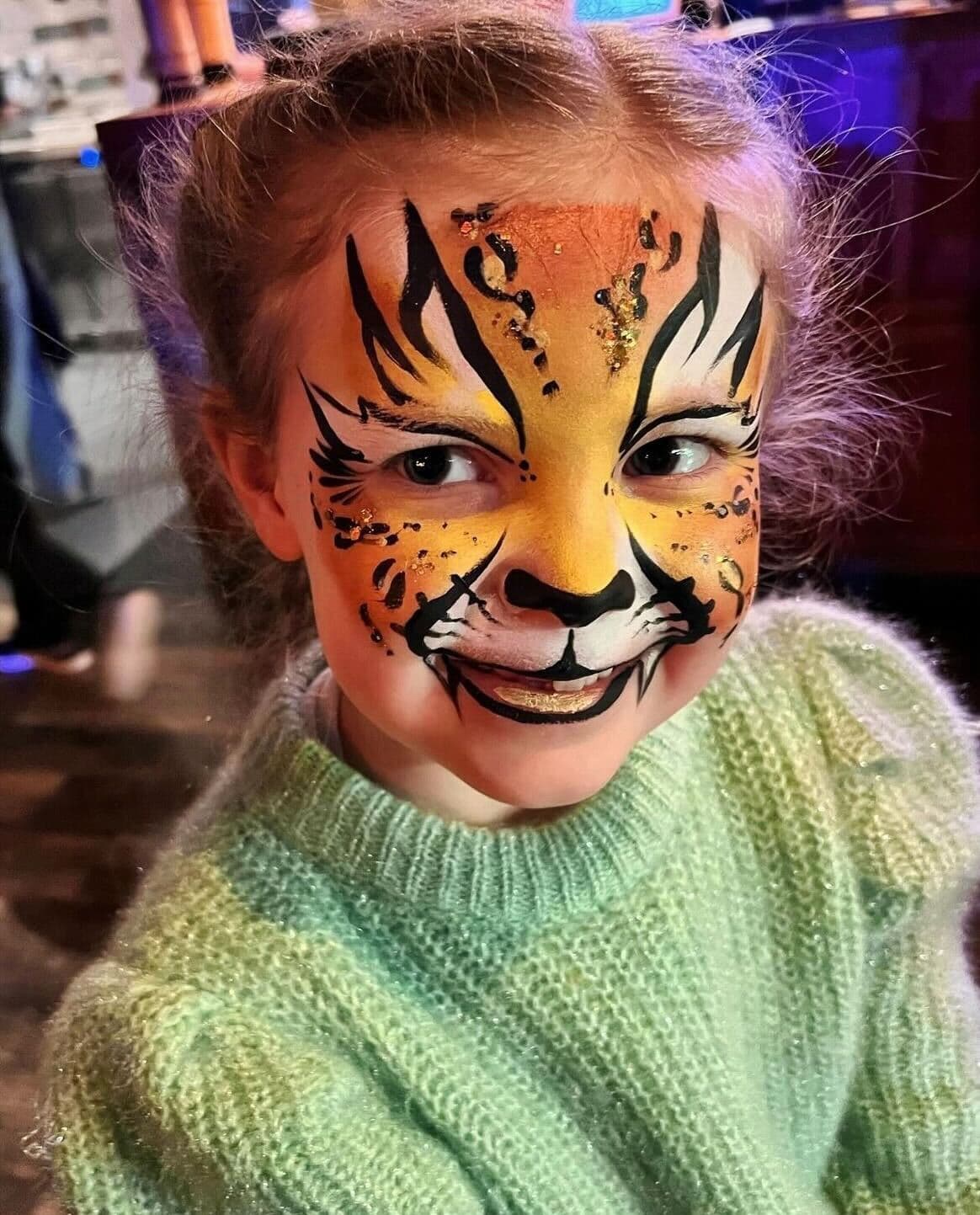 A child smiling with her face painted like a lion.