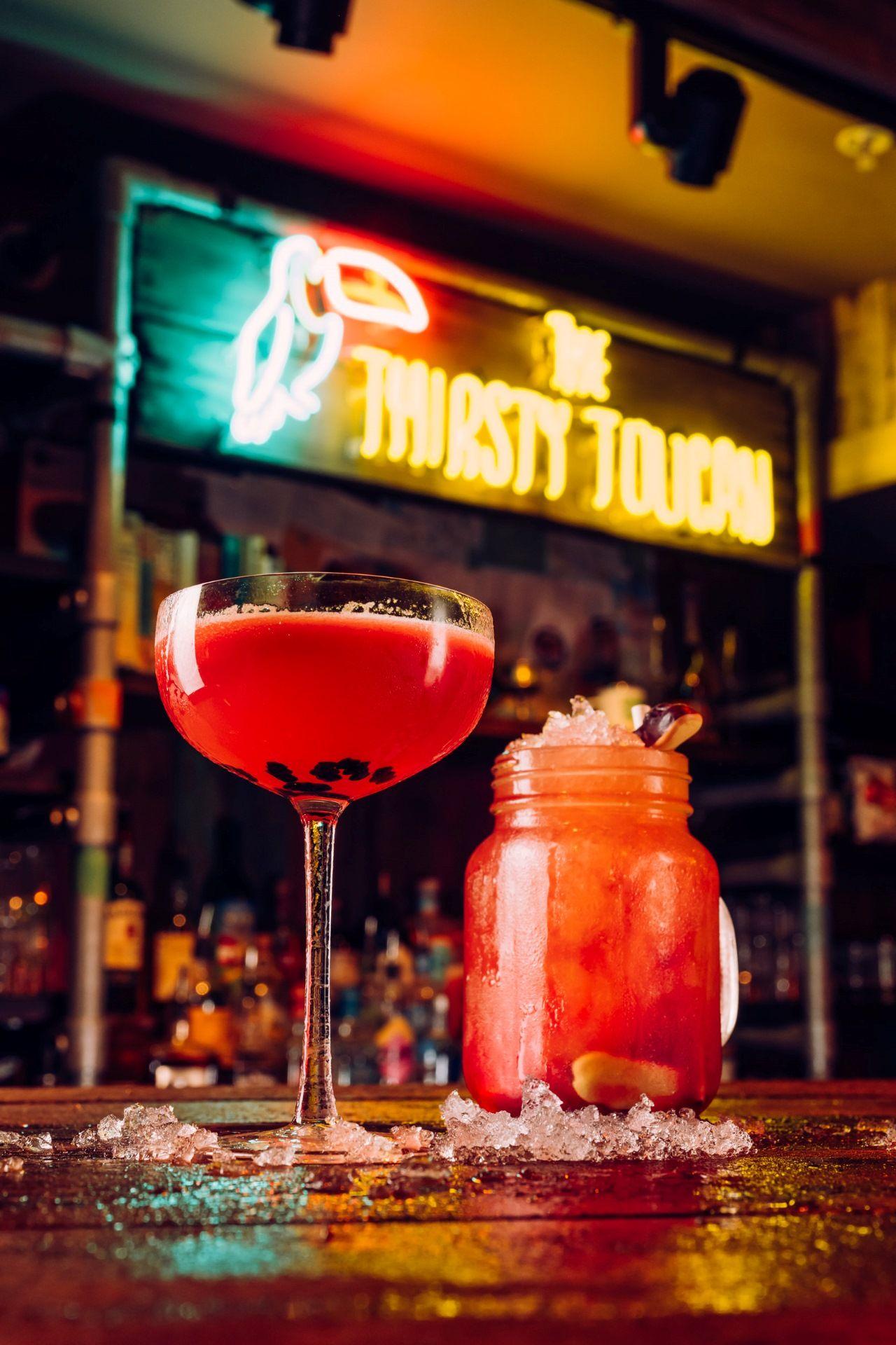 Two cocktails positioned in front of The Thirsty Toucan Sign