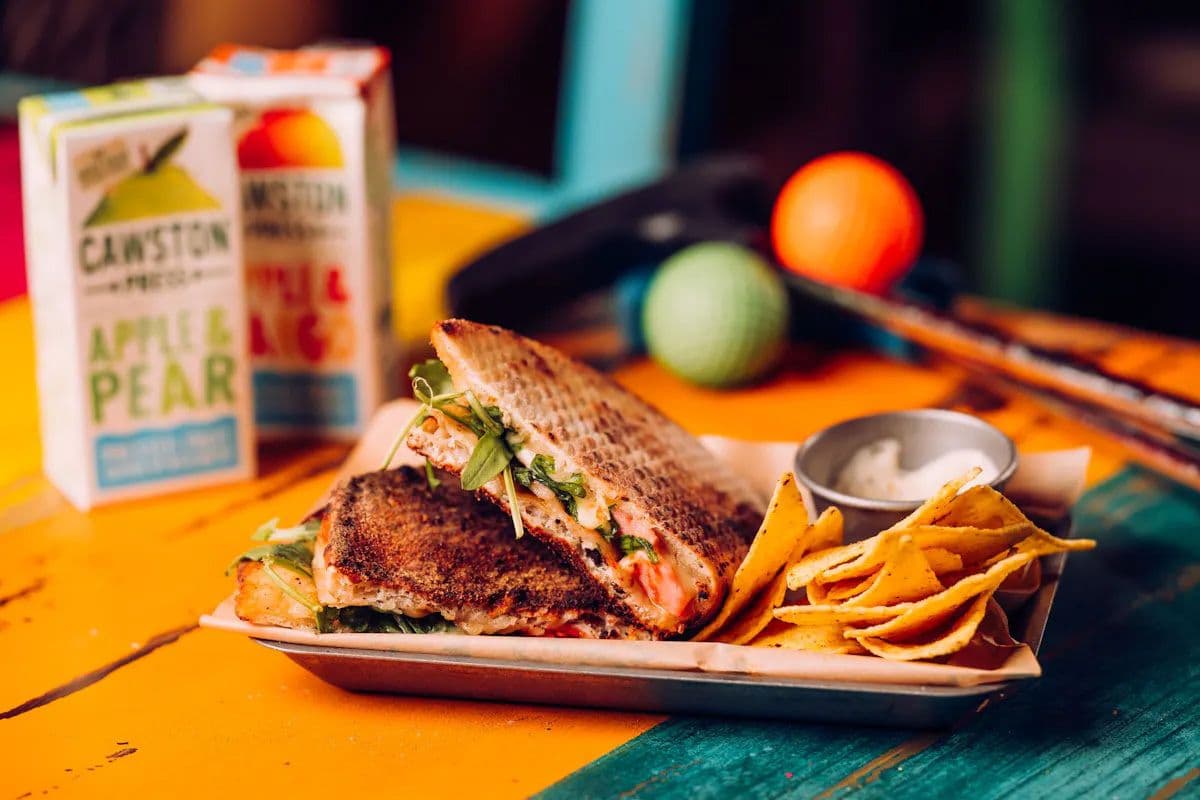 A Treetop Melt sandwich at Treetop Golf displayed with cartons of juice and mini golf equipment.