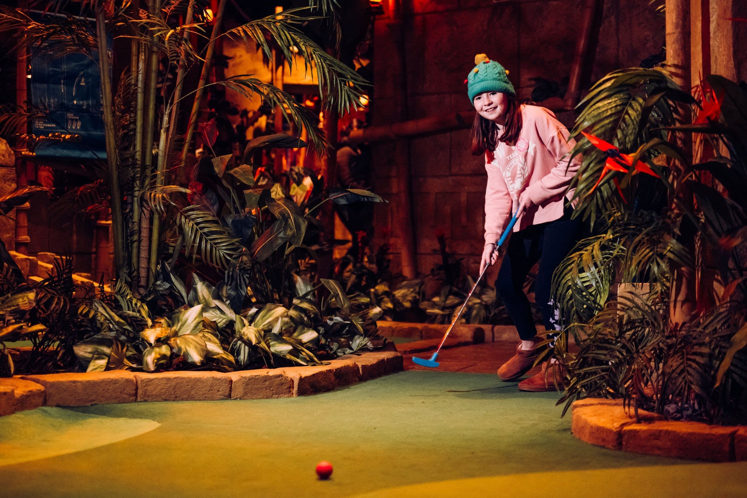 A young girl wearing a woolie hat playing mini golf