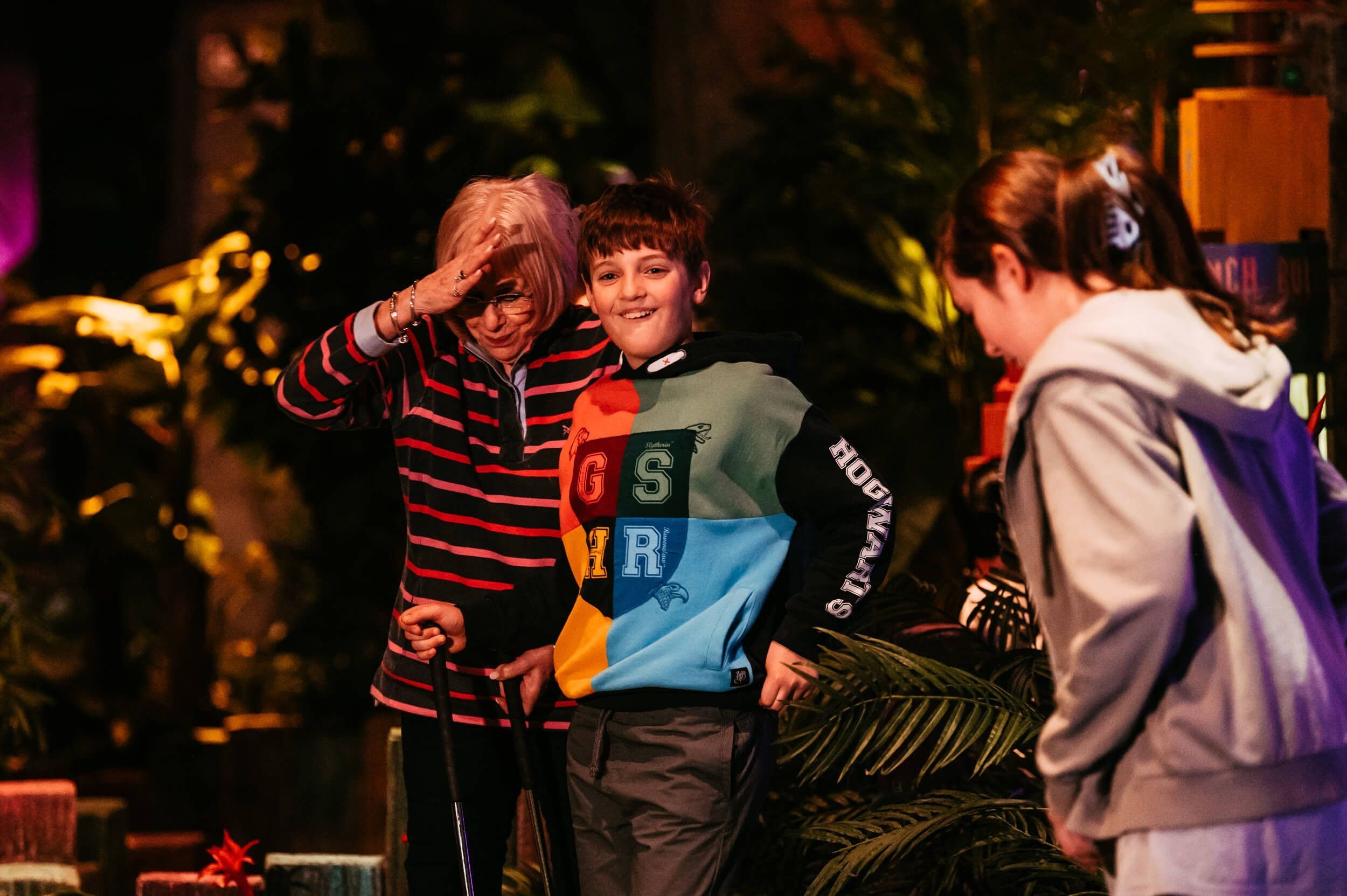 A young boy wearing a Harry Potter sweatshirt and his family roam the Treetop jungle with their mini golf clubs in hand.