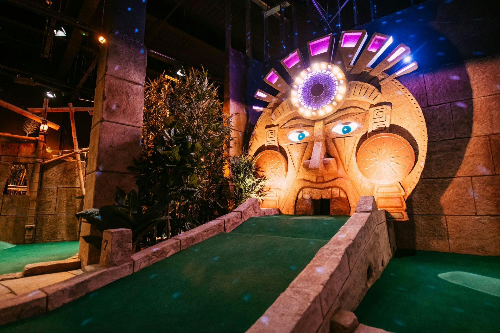 Mini golf green run-up to the Fabulous Sacred Mask’s large gold structure, with big glowing eyes and a pink jewel-encrusted crown. 