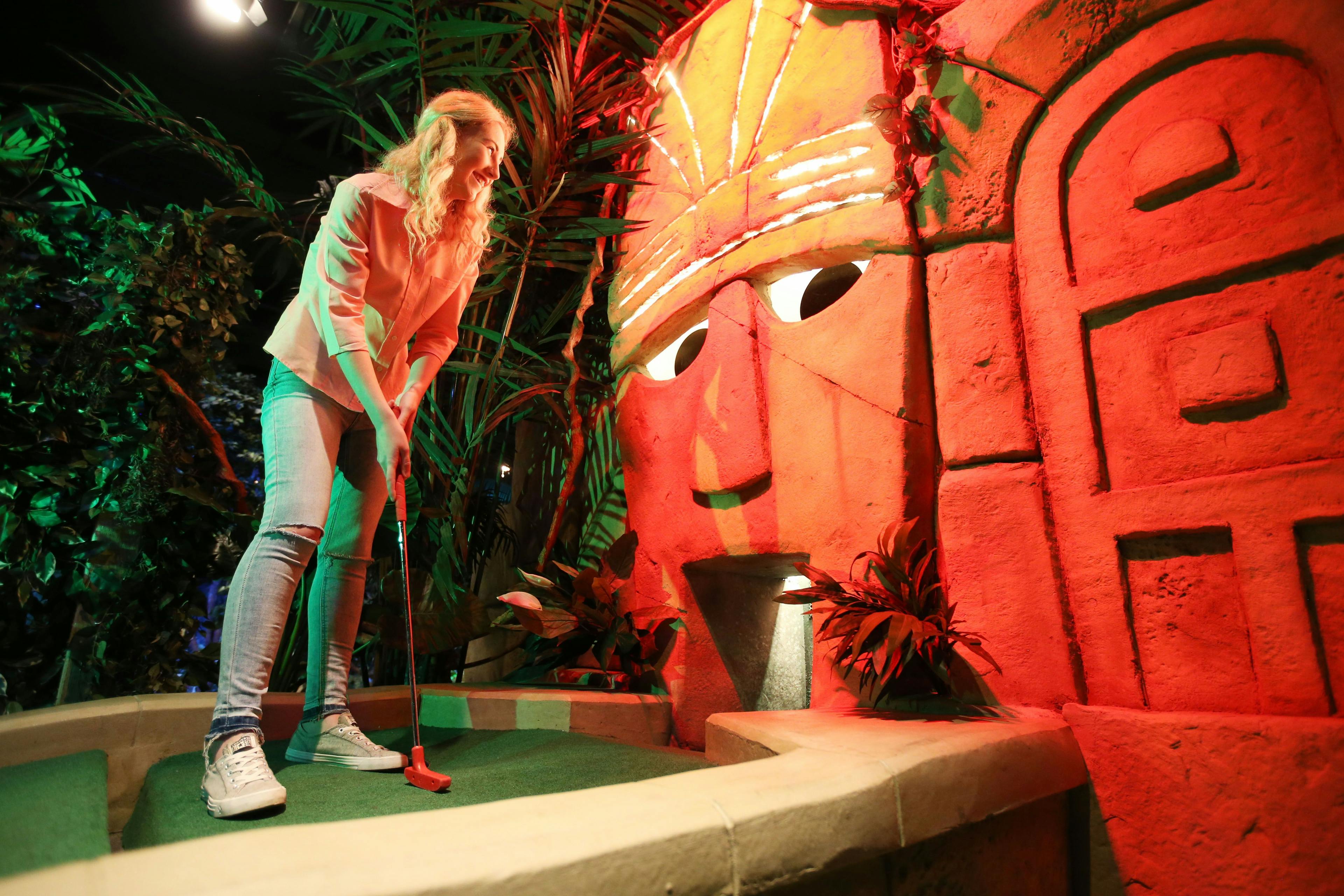 A young girl with blonde hair hitting her ball into the Fabulous Sacred Masks mouth, while his big black eyes stare back and golden crown glows. 