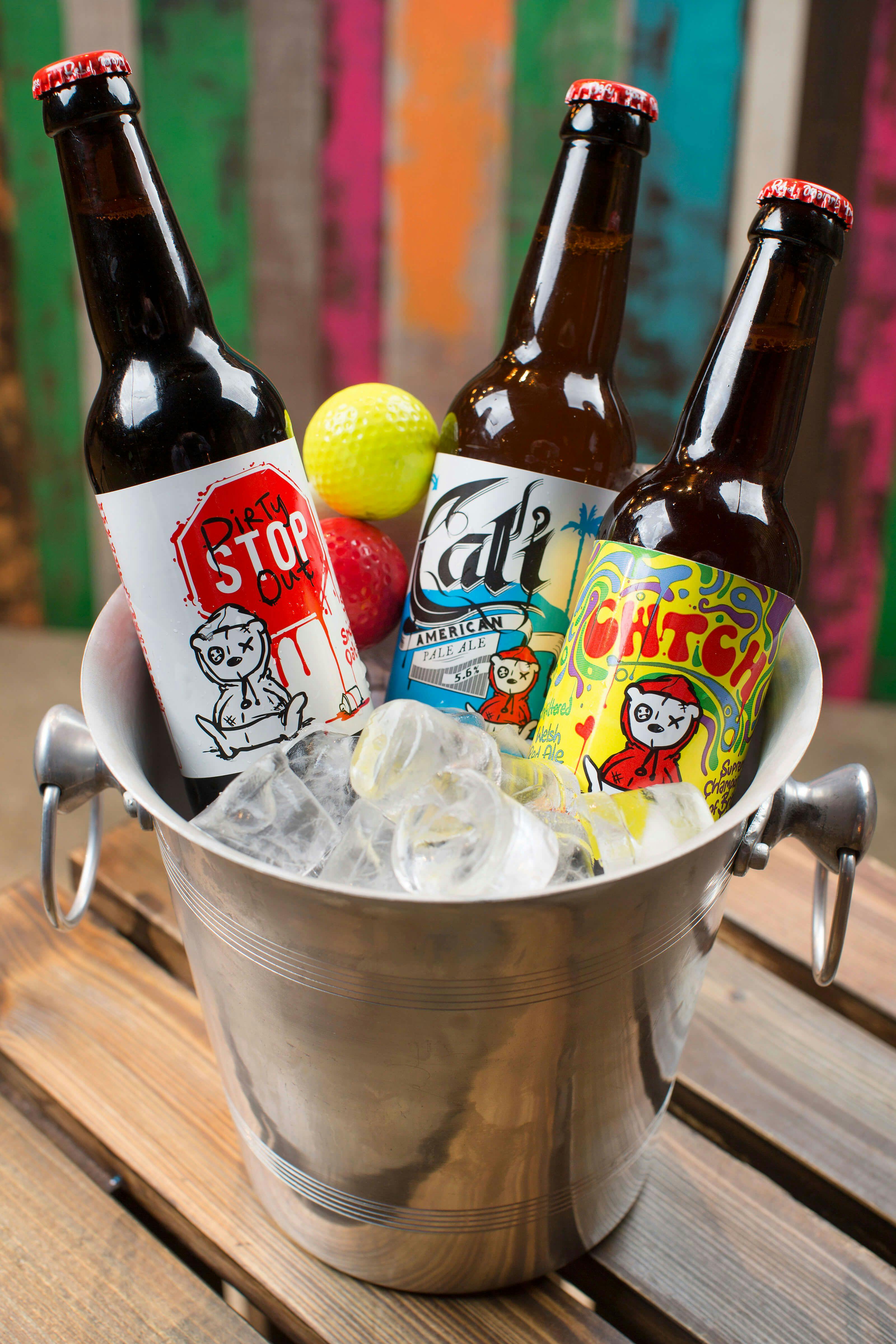 A selection of cold, local craft beer sit in a metal bucket of ice on a wooden table. 
