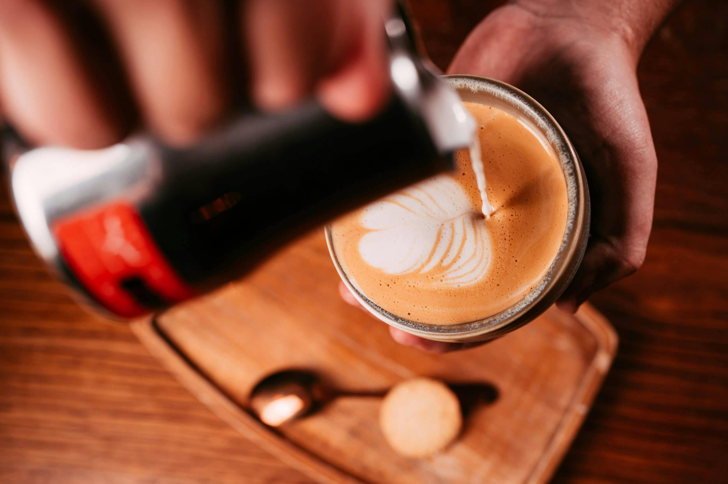 Image of a latte being poured from above, with rich white milk being tipped at height into a mug.