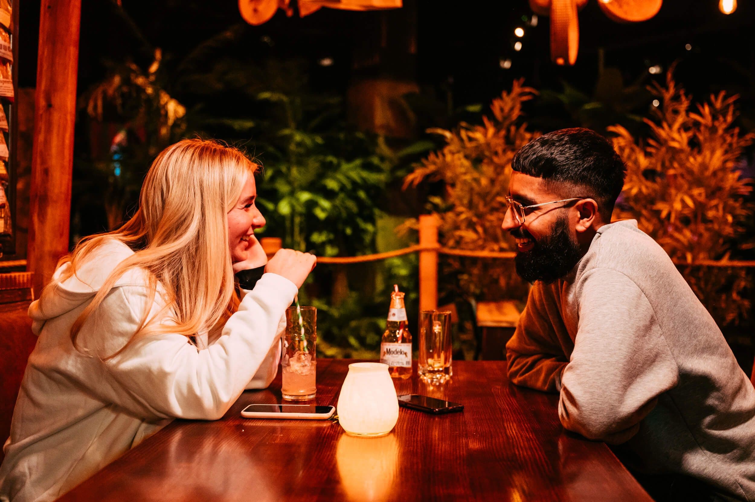 Happy couple enjoy tropical cocktails and a beer at a wooden table in the Thirsty Toucan Bar.