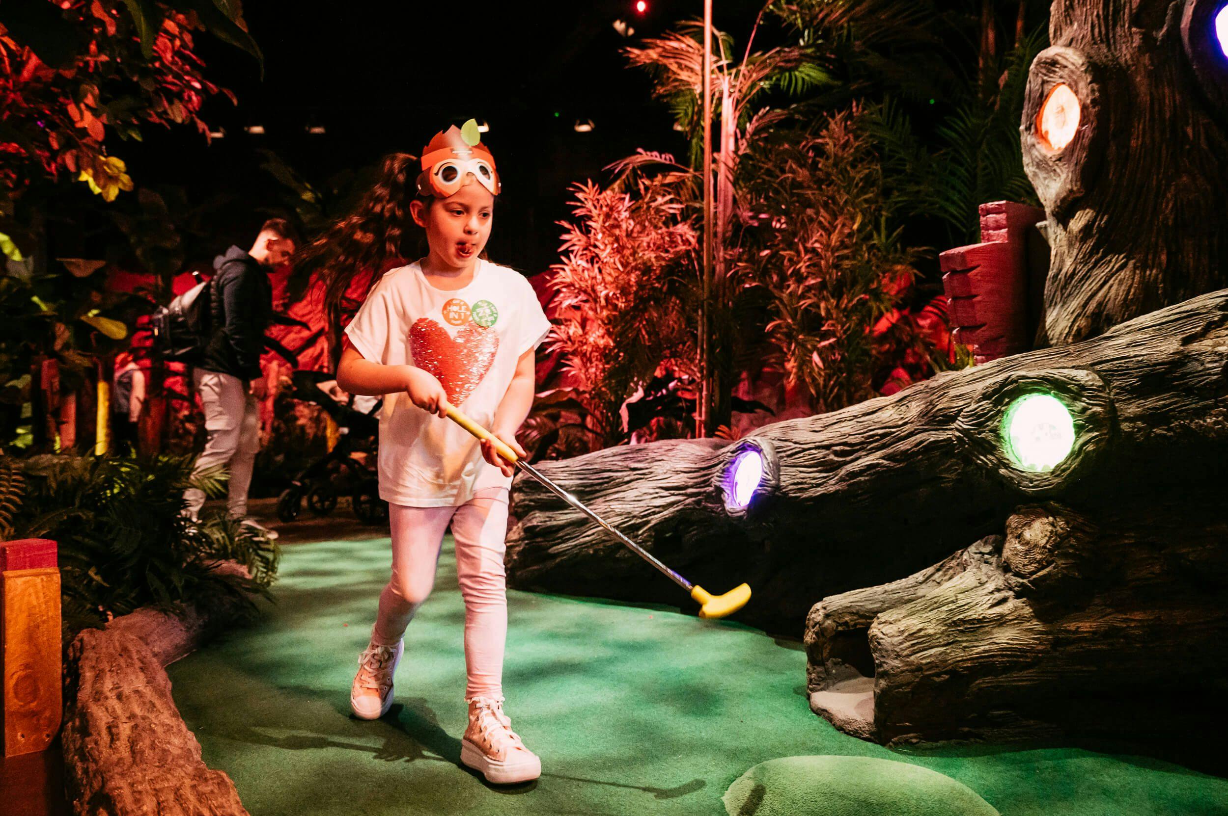 Young girl wearing a monkey mask running through the Mystic Woods with a mini golf club in her hand.
