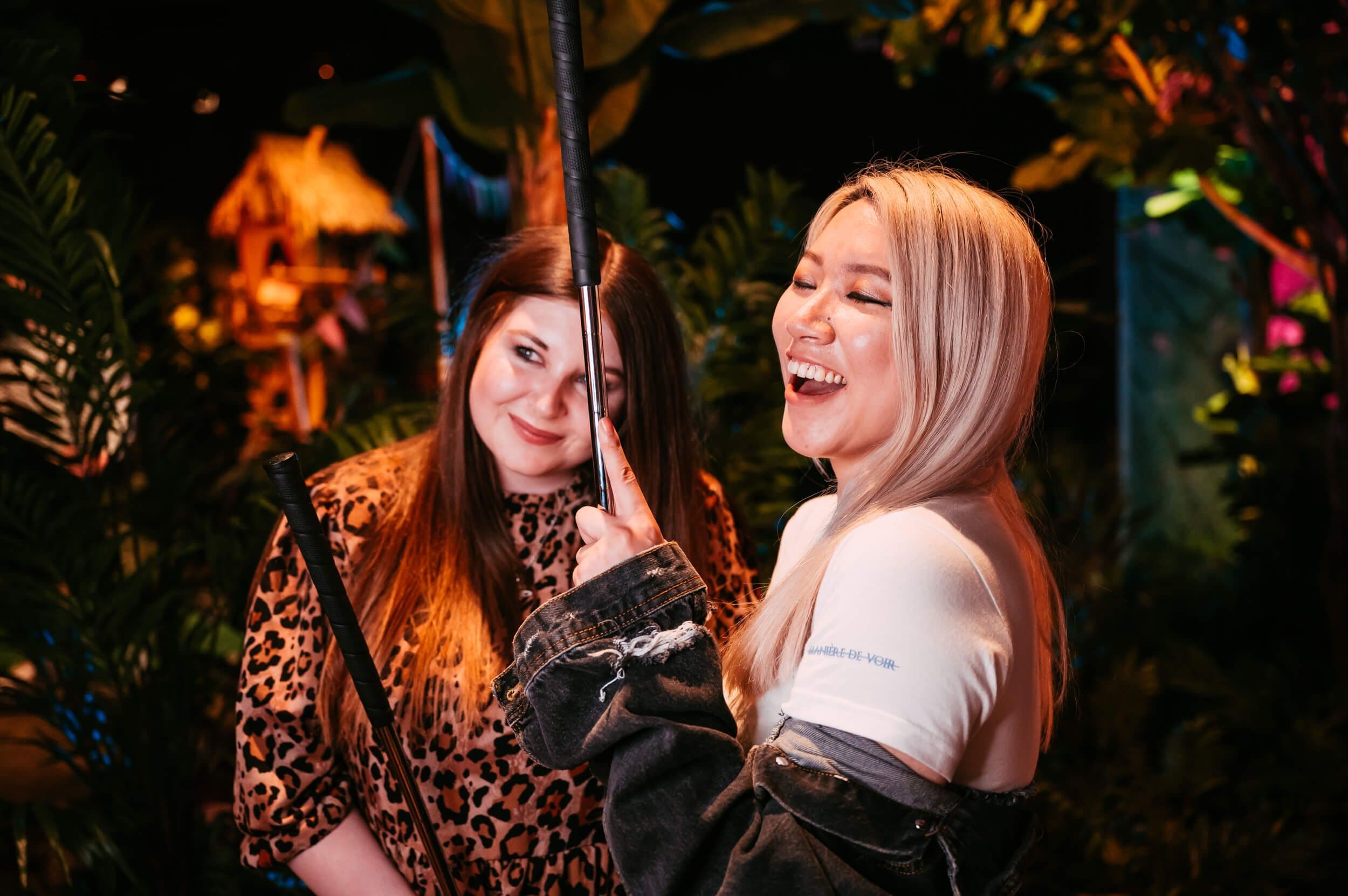 Two women laughing as they hold their mini golf clubs up in the Treetop rainforest.