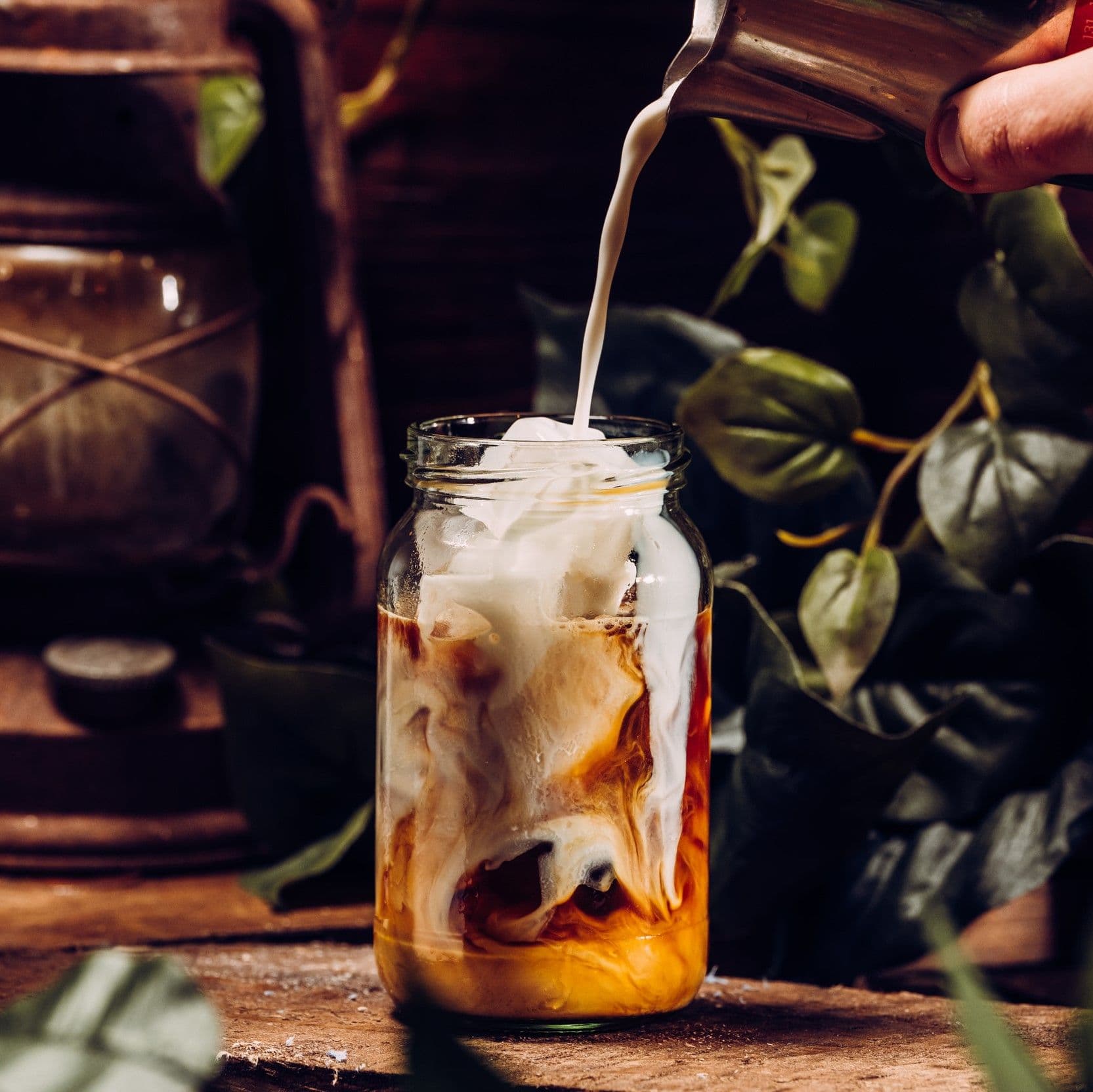 A close up image of milk being poured into an ice coffee.