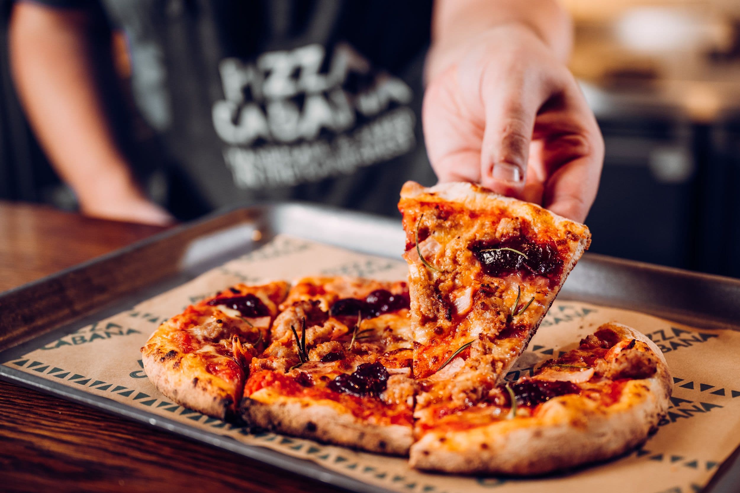 Chef holding a slice of the pigs n blankets pizza.