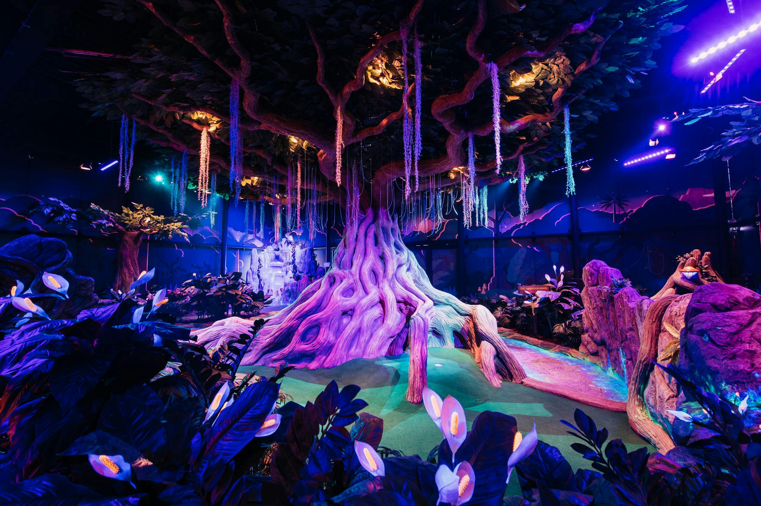 A wide-angle image of the Mighty Oracle Tree, with bright twisting vibes and large tangling roots looping through the mini golf jungle.