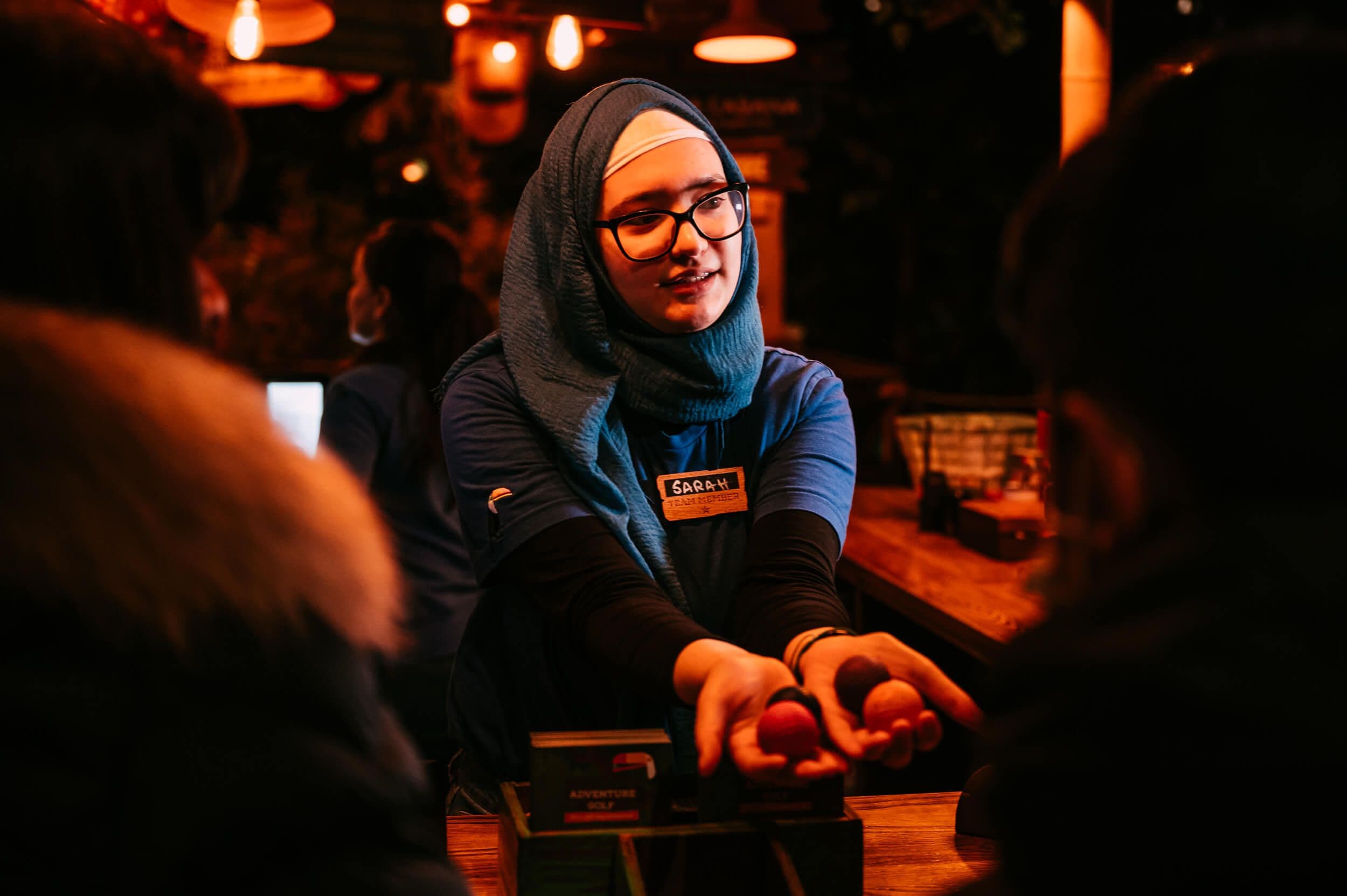 Helpful Treetop visitor guide with blue headscarf handing players their mini golf balls.