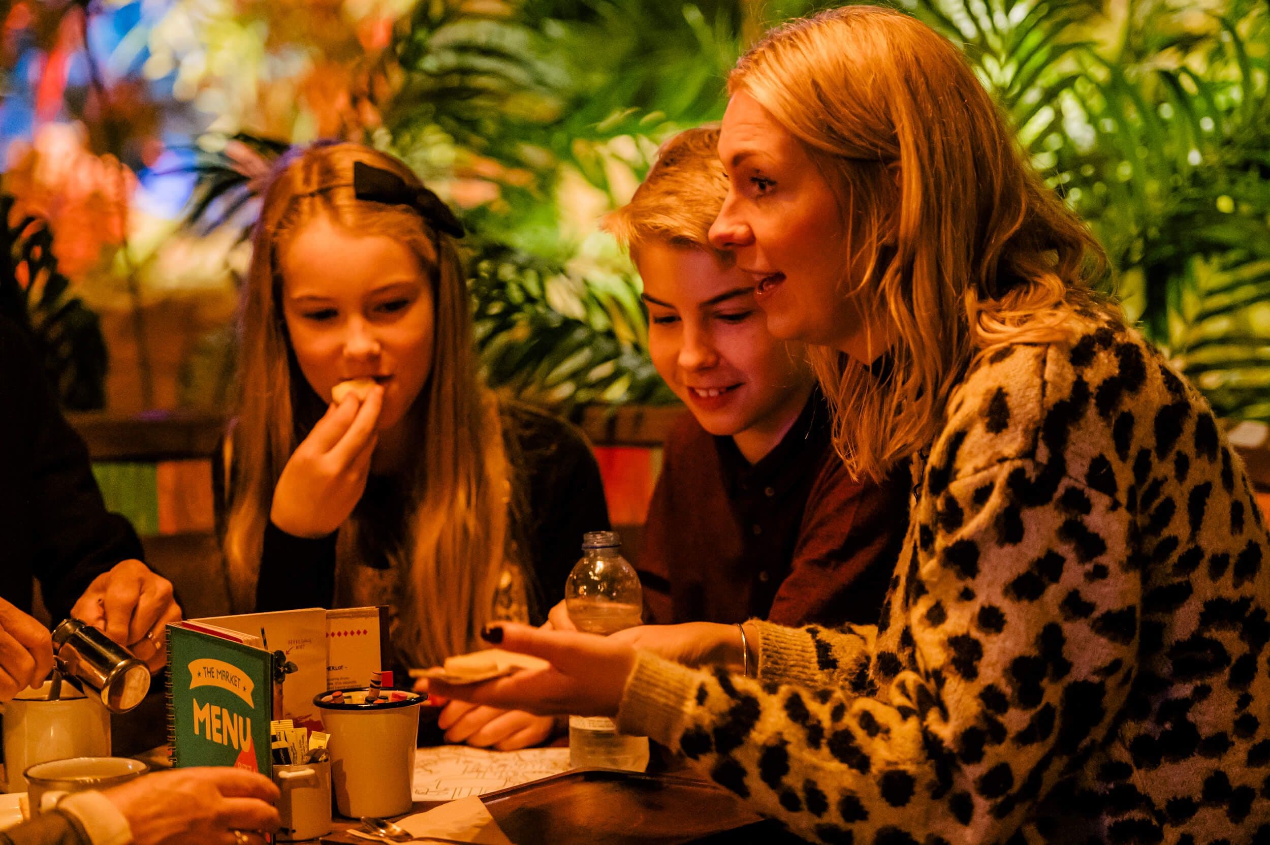 A family sit together around a table eating a pizza from the Pizza Cabana, smiling and laughing. 