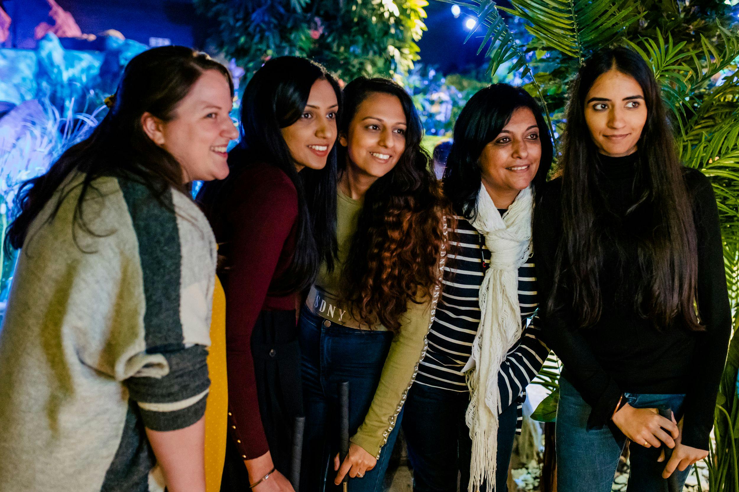 Five women wearing jeans and neutral colours smile for the free photobooth, hugging each other in a line.