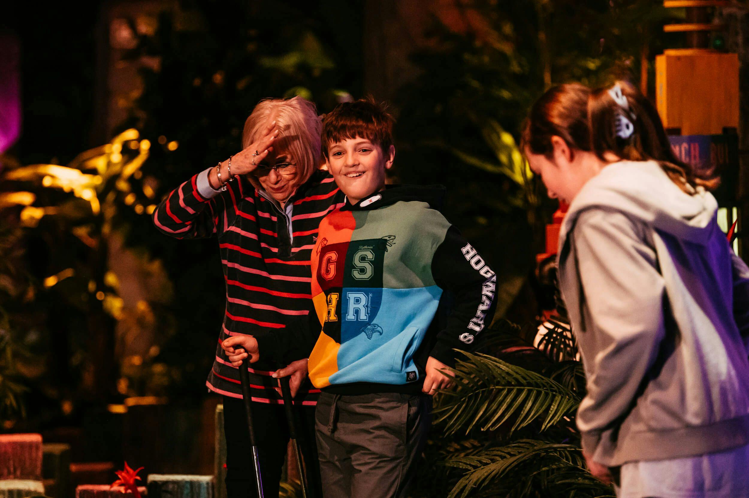 A young boy wearing a Harry Potter sweatshirt and his family roam the Treetop jungle with their mini golf clubs in hand. 