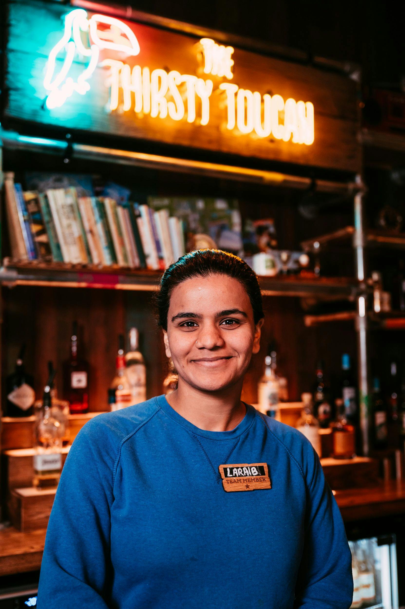 Treetop employee in a blue shirt smiles at the camera from within the Thirsty Toucan Bar.