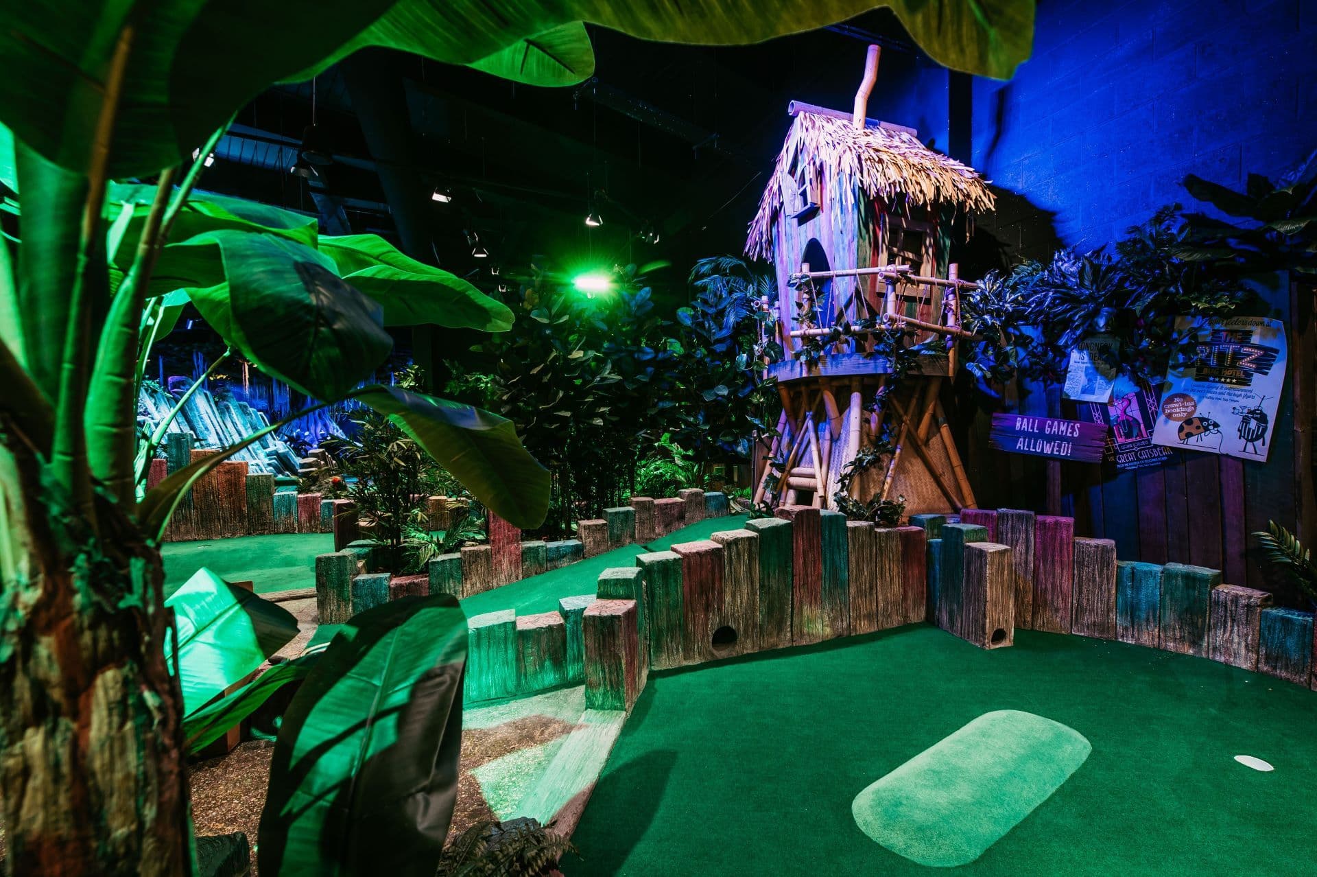 Bright image of the Twee-T Tower birdhouse hole, with a large wooden green and red house, thatched roof and thick jungle foliage around. 