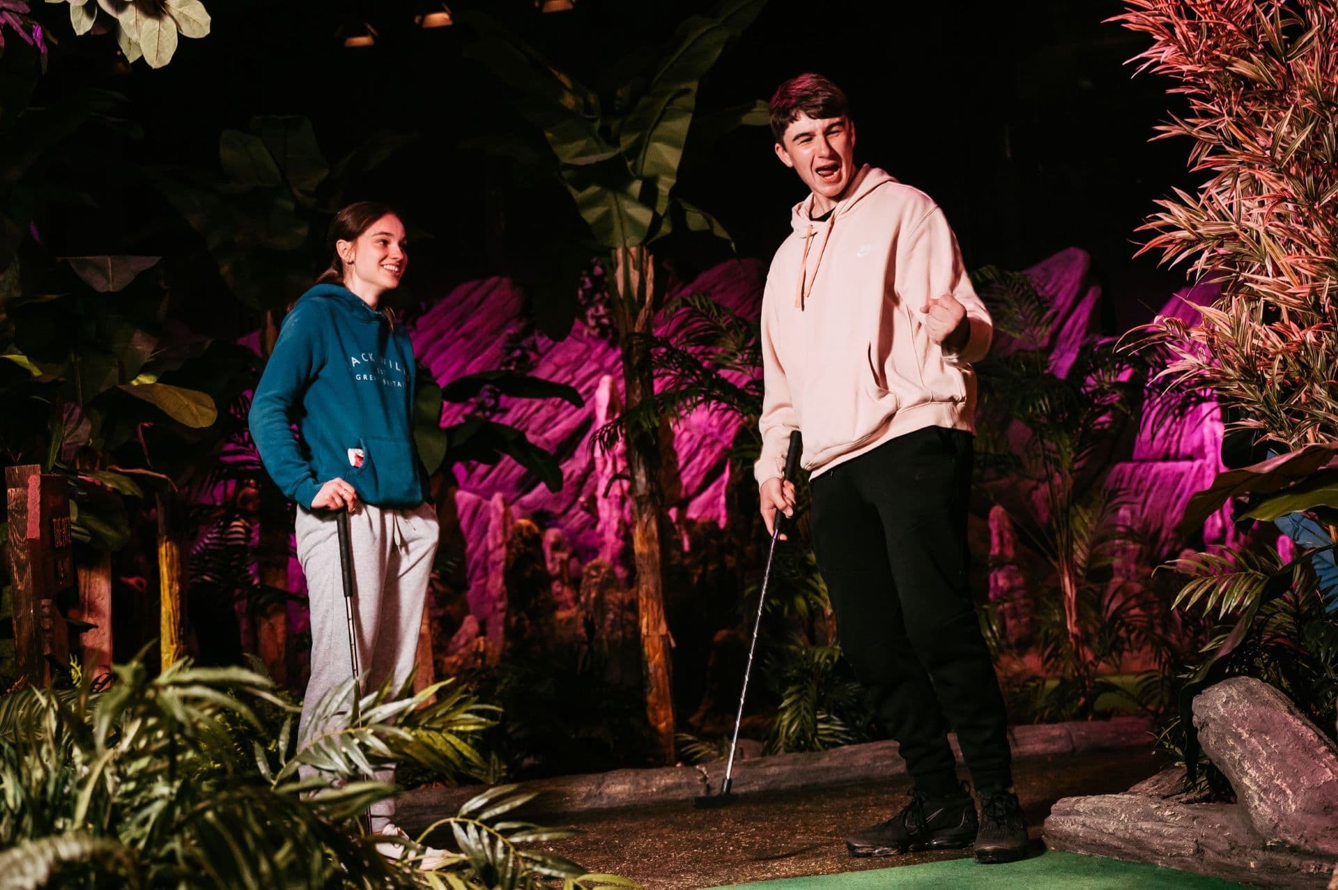 Two young adults smile and watch the golf ball.